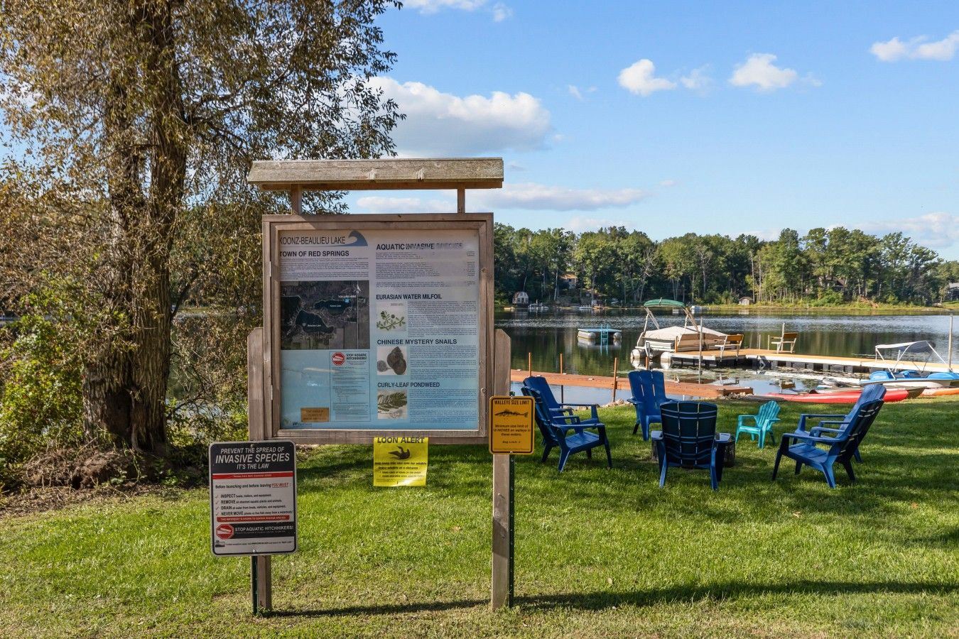 A lakeside informational sign with a view of a dock and chairs.