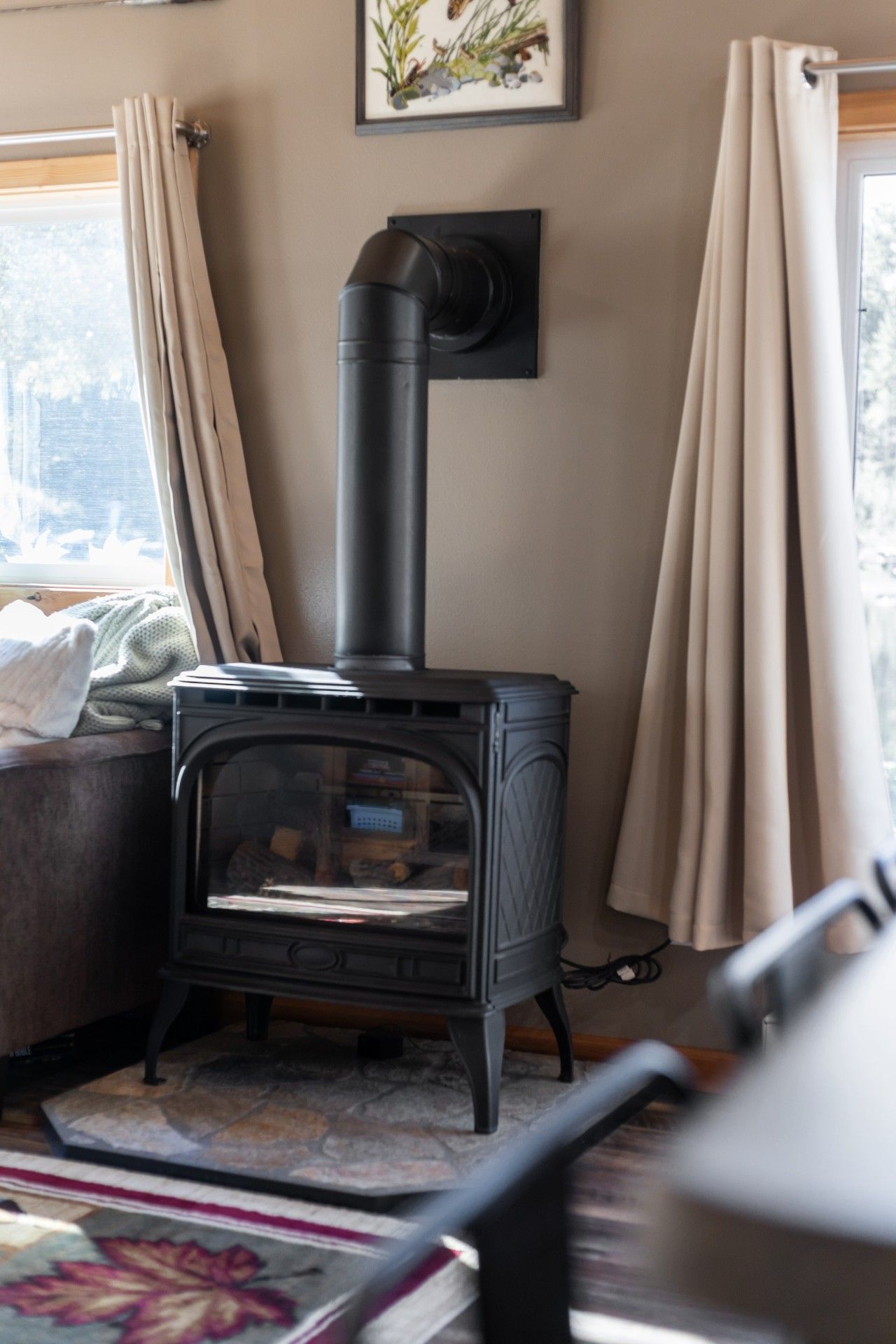 A room with a black wood-burning stove, beige curtains, and a framed picture on the wall.