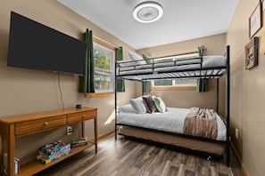 A bunk bed room with a desk, a television, and a window with curtains.