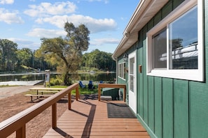 A wooden deck with a bench and chairs, a small table, and a view of a lake with trees.