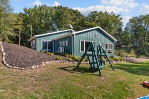 A two-story house with a green exterior, a swing set in the yard, and a small deck. - Lake Front! Private Dock! Water toys! (Gresham)
