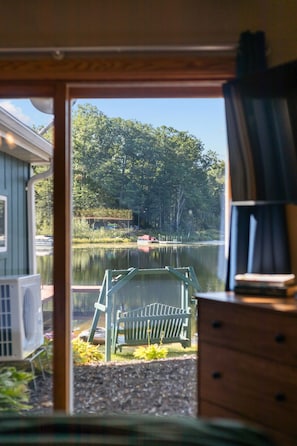 A view from inside a cabin looking out to a lake with a dock and a boat, surrounded by trees.