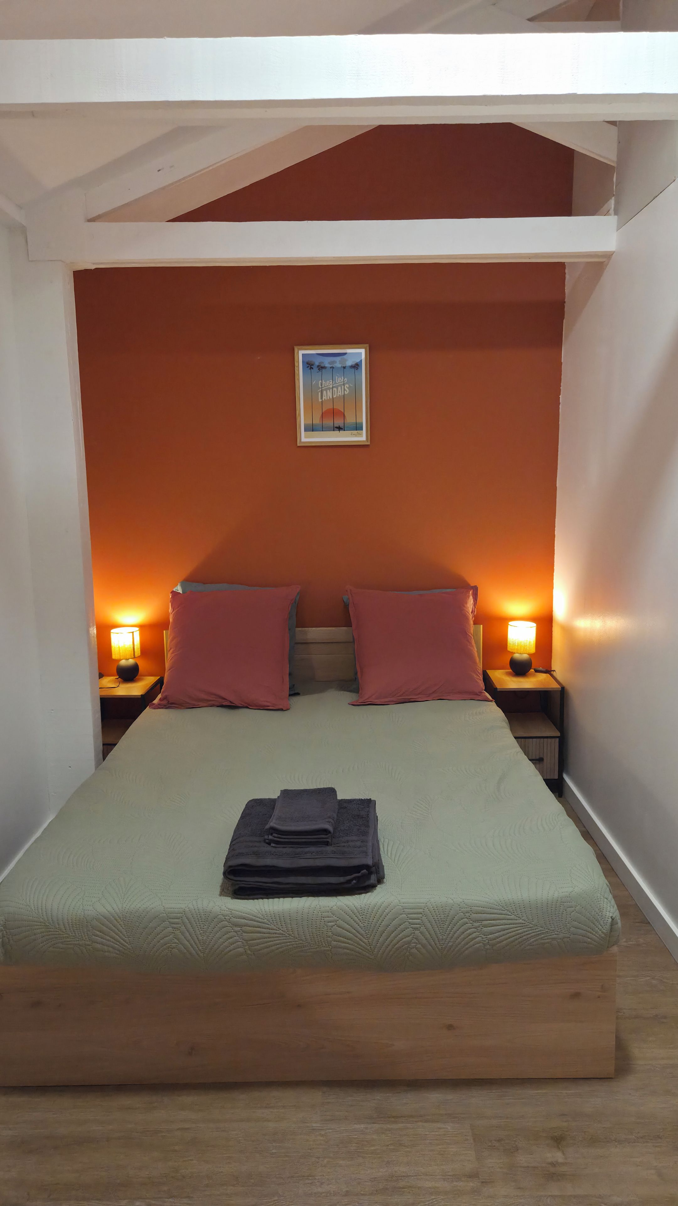 A single bed with a headboard, two bedside lamps, and a folded towel on the bed.