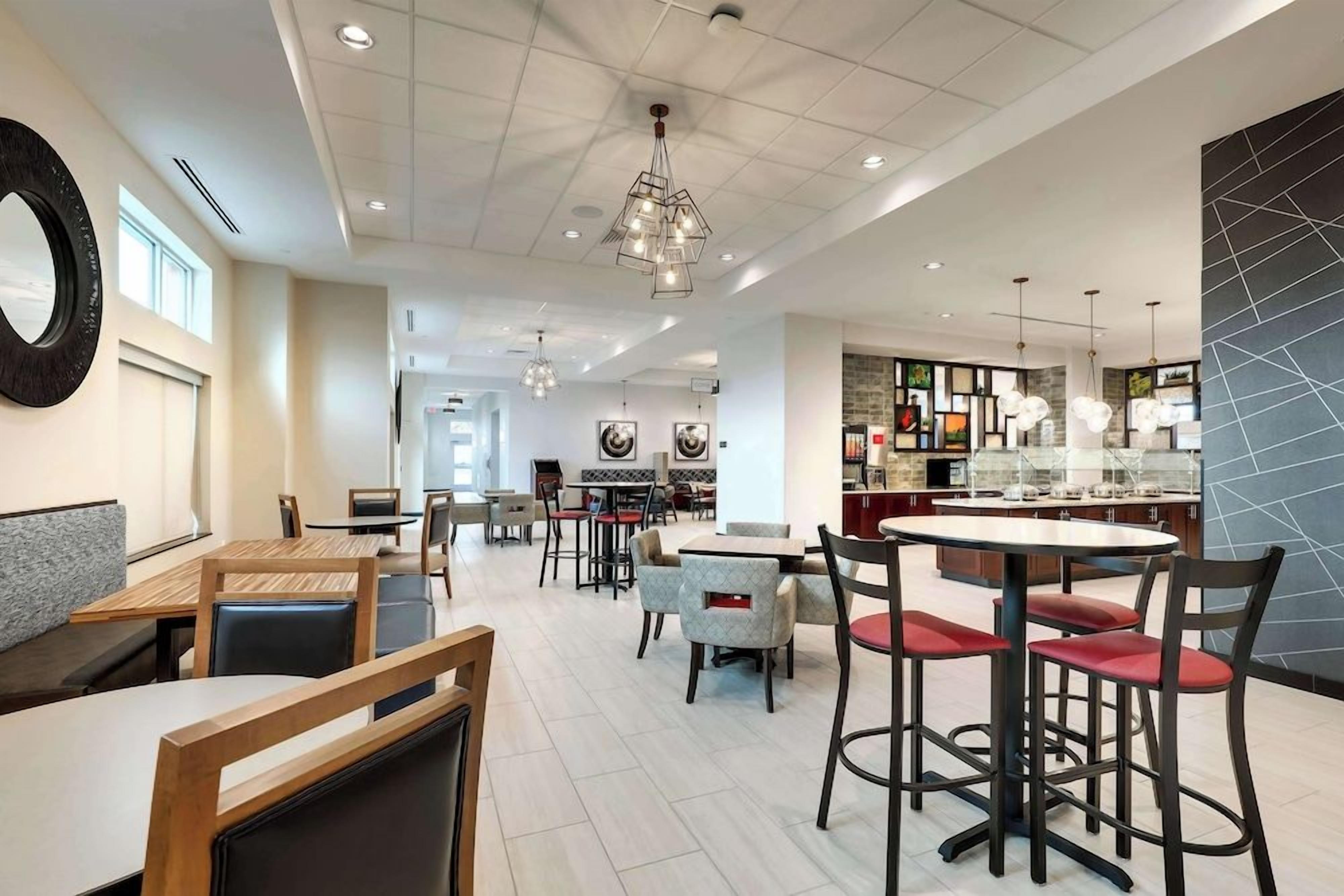 A modern dining area with multiple seating options, including booths and tables, and a kitchen area visible in the background.