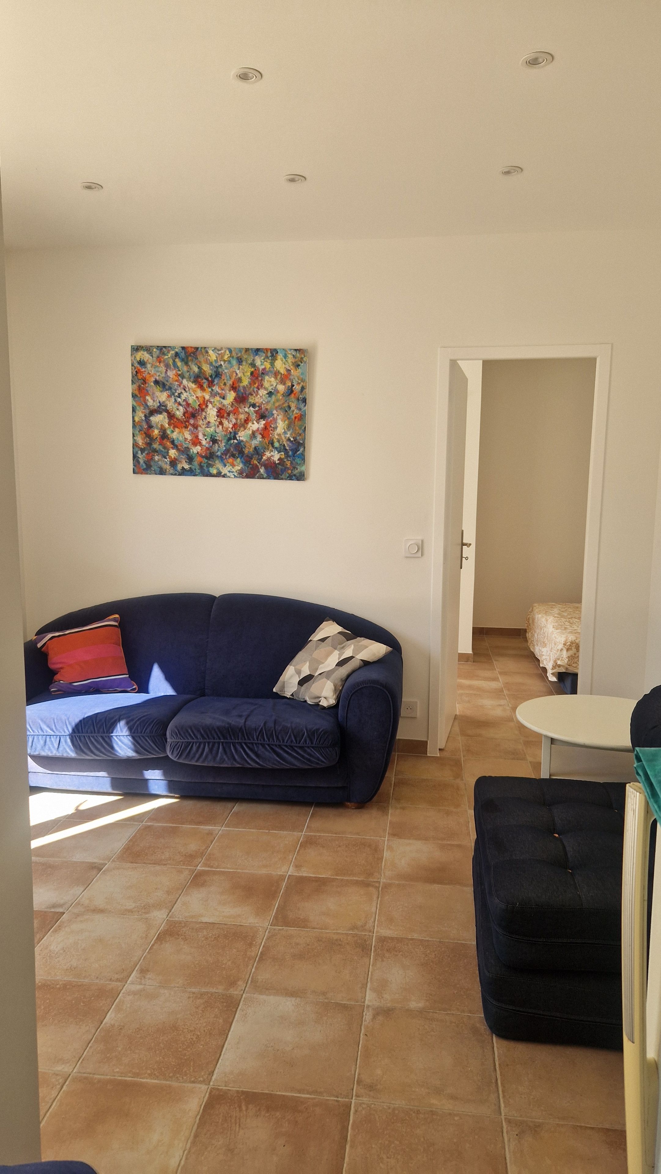 Un salon avec un canapé bleu foncé, un tableau abstrait aux couleurs vives et un sol carrelé.