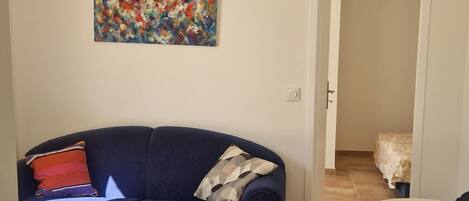Un salon avec un canapé bleu foncé, un tableau abstrait aux couleurs vives et un sol carrelé.