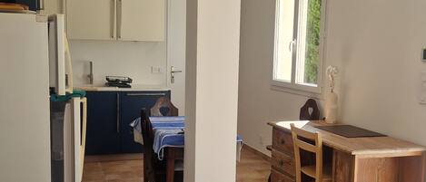 A spacious living area with a dining table, a kitchen in the background, and a large window providing natural light.