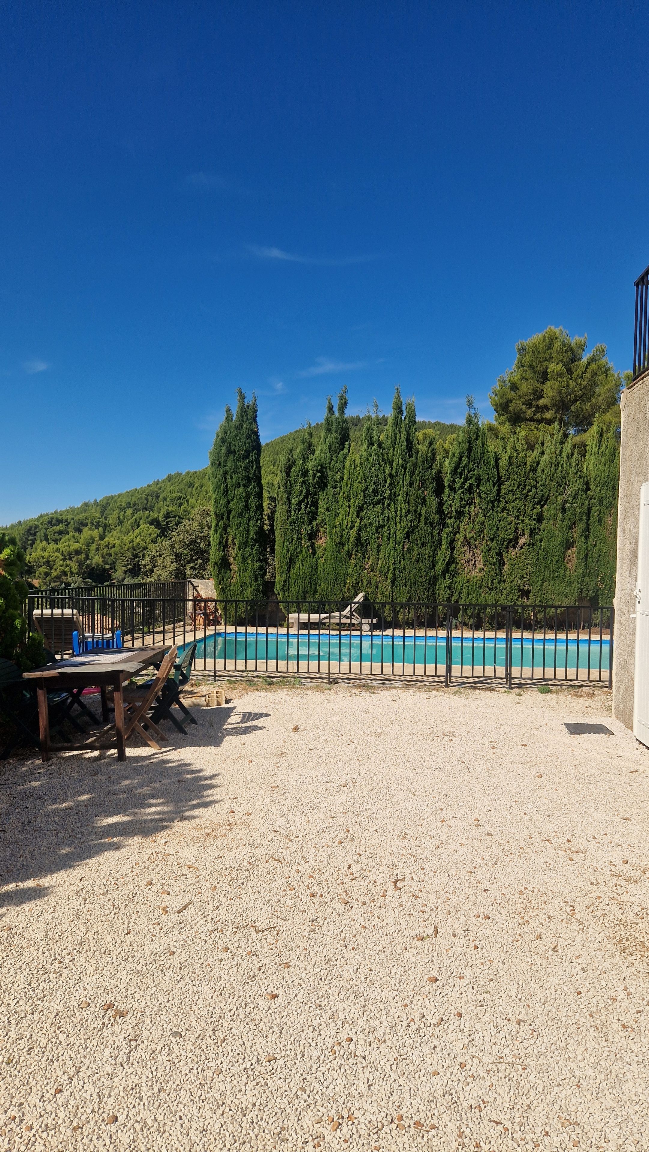 Un espace piscine avec un sol en gravier, une terrasse en bois et une clôture en métal.
