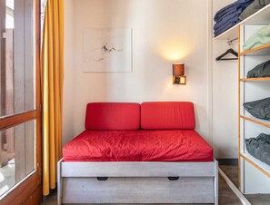 A compact bed with a red cover, a wall-mounted light, and a framed picture above it. - Alpine Stay With Balcony in Tignes (Tignes)