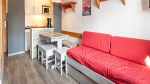 Un espacio habitable compacto con kitchenette, una zona de comedor con mesa y sillas, y un sofá rojo.