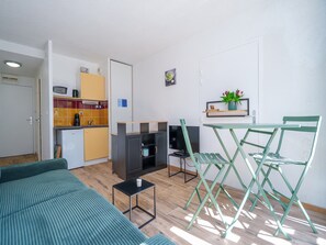 Un espacio habitable compacto con kitchenette, un sofá, una mesa de comedor con sillas y un televisor.