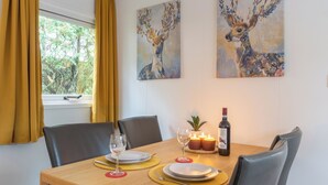 A dining area with a wooden table set for two, two paintings on the wall, and a window with curtains. - Vrbo Property (Putten)