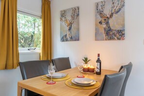 Een eetgedeelte met een houten tafel gedekt voor twee personen, twee schilderijen aan de muur en een raam met gordijnen.