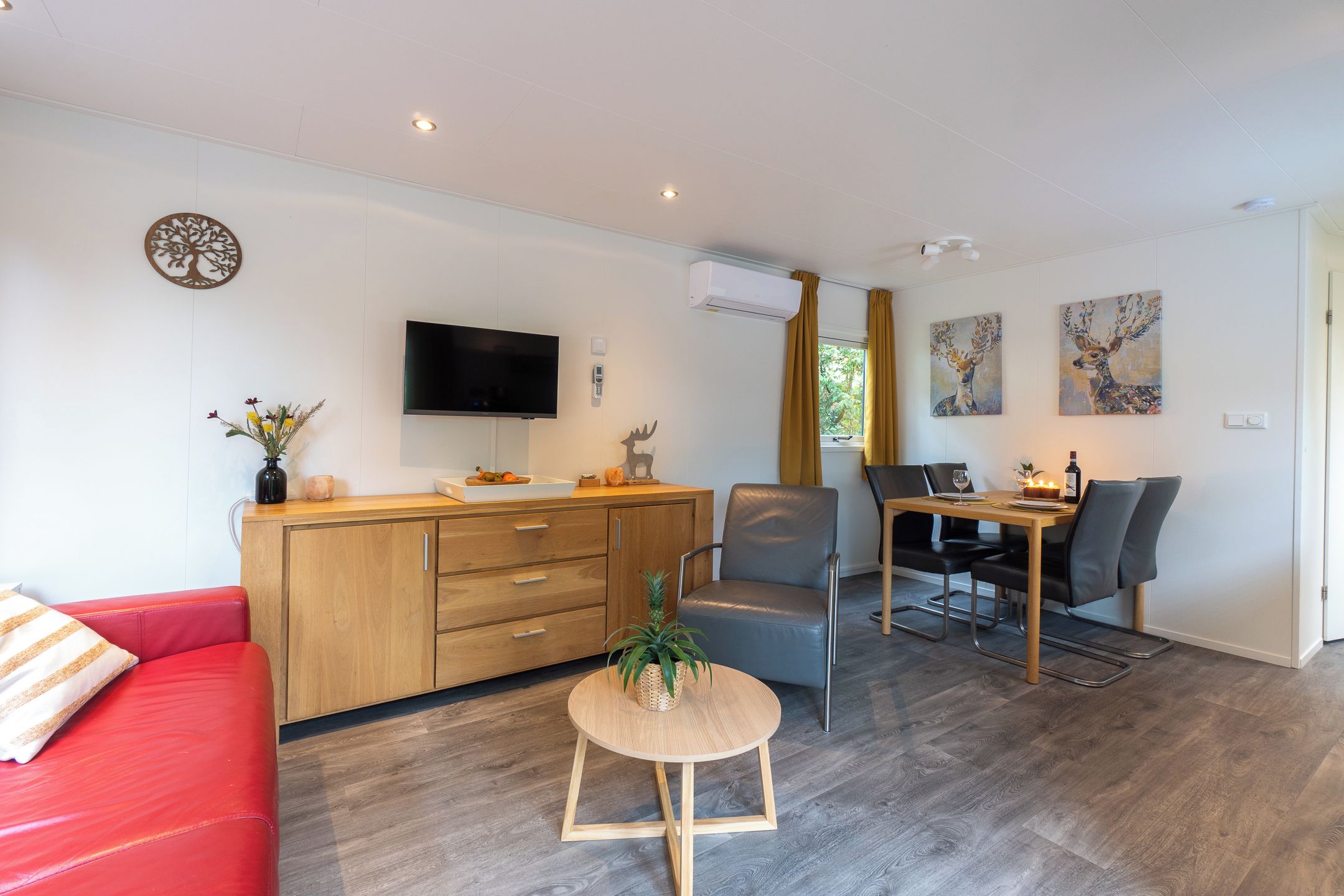 Un salon moderne avec un canapé rouge, un meuble en bois, une télévision et un coin repas comprenant une table et des chaises.