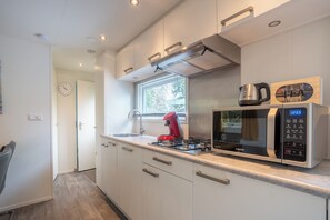Une cuisine moderne avec des meubles blancs, un four à micro-ondes en acier inoxydable, une bouilloire rouge et une fenêtre avec des stores.