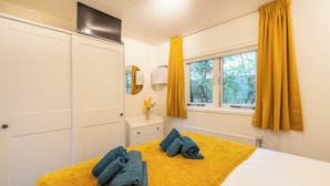 A hotel room with a bed, a window with curtains, a mirror, and a radiator. - Vrbo Property (Putten)