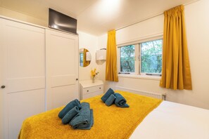Een hotelkamer met een bed, een raam met gordijnen, een spiegel en een radiator.