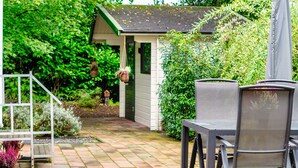 A patio area with a table and chairs, a small shed, and lush greenery. - Vrbo Property (Putten)