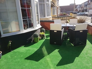 An outdoor seating area with a table and chairs, a small potted plant, and a window with curtains. - Sheron House Bed & Breakfast (Blackpool)