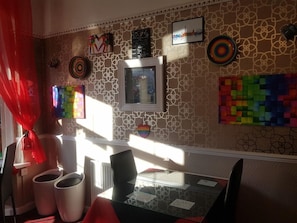 A room with a patterned wall, a framed picture, a colorful abstract artwork, and a window with sunlight. - Sheron House Bed & Breakfast (Blackpool)