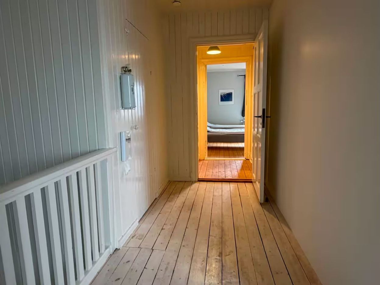 Un corridoio con pavimento in legno e pareti bianche, che conduce a una stanza con un letto.