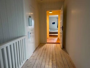 A hallway with wooden flooring and white walls, leading to a room with a bed.