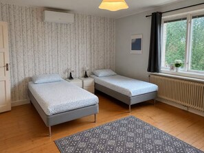 A bedroom with two beds, a radiator, a window with curtains, and a patterned rug.