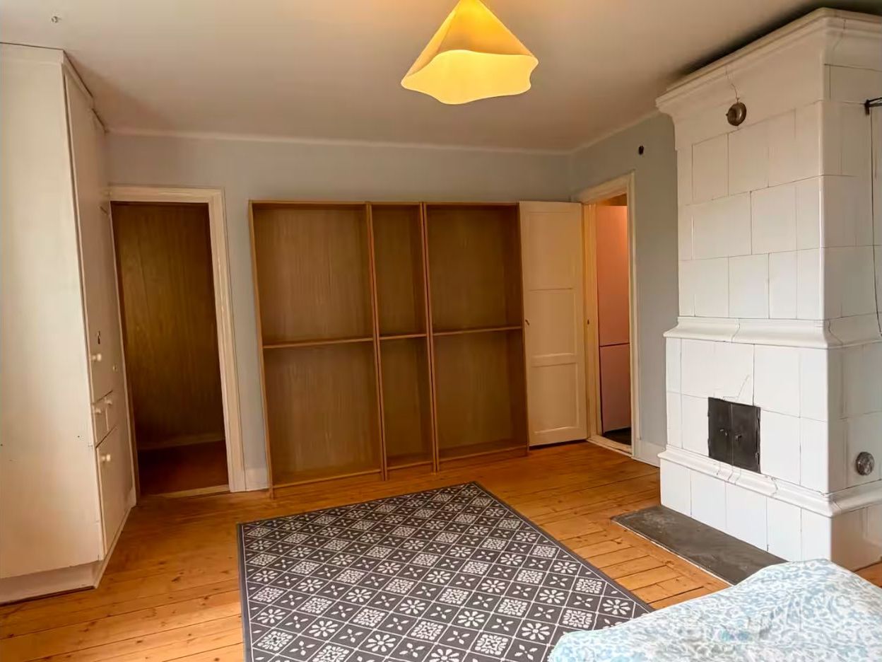 A room with a wooden floor, a patterned rug, a white fireplace, and a sliding door closet.