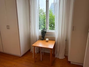 A room with a wooden floor, a table with a candle, and a window with curtains.