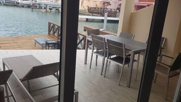 A balcony with a view of a marina, a table with chairs, and a wooden deck.