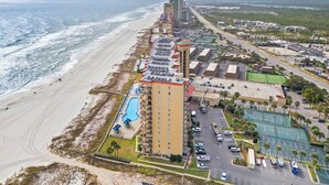 Et kysthotel med en lang bygning langs stranden, en swimmingpool og en tennisbane.