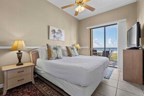 A hotel room with a bed, nightstands, a ceiling fan, a painting, a television, and a balcony with a view. - 🌊 Beachfront Gulf Views | Indoor & Outdoor Pools | Phoenix V 116 (Orange Beach)