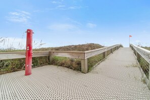 A wooden boardwalk leading to a beach with a red post and a flag. - 🌊 Beachfront Gulf Views | Indoor & Outdoor Pools | Phoenix V 116 (Orange Beach)