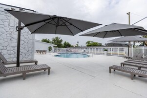Zona de piscina con sillas de descanso y sombrillas, un muro de piedra y una piscina cercada.