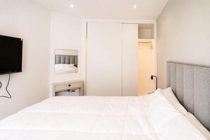 A bedroom with a bed, a bedside table, a mirror, and a wardrobe.