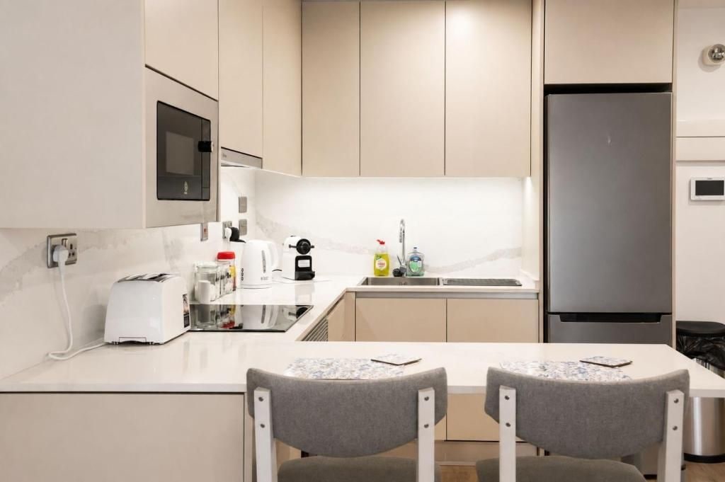 Una cocina moderna con microondas incorporado, refrigerador de acero inoxidable y un pequeño comedor con dos sillas.