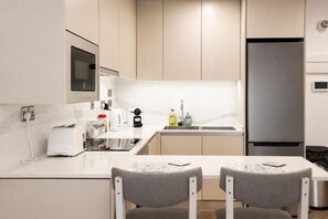 A modern kitchen with a built-in microwave, a stainless steel refrigerator, and a small dining area with two chairs.