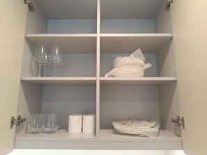A cabinet with shelves containing wine glasses, plates, and napkins. - Executive Suite with Swimming Pool & Gym (Gibraltar)