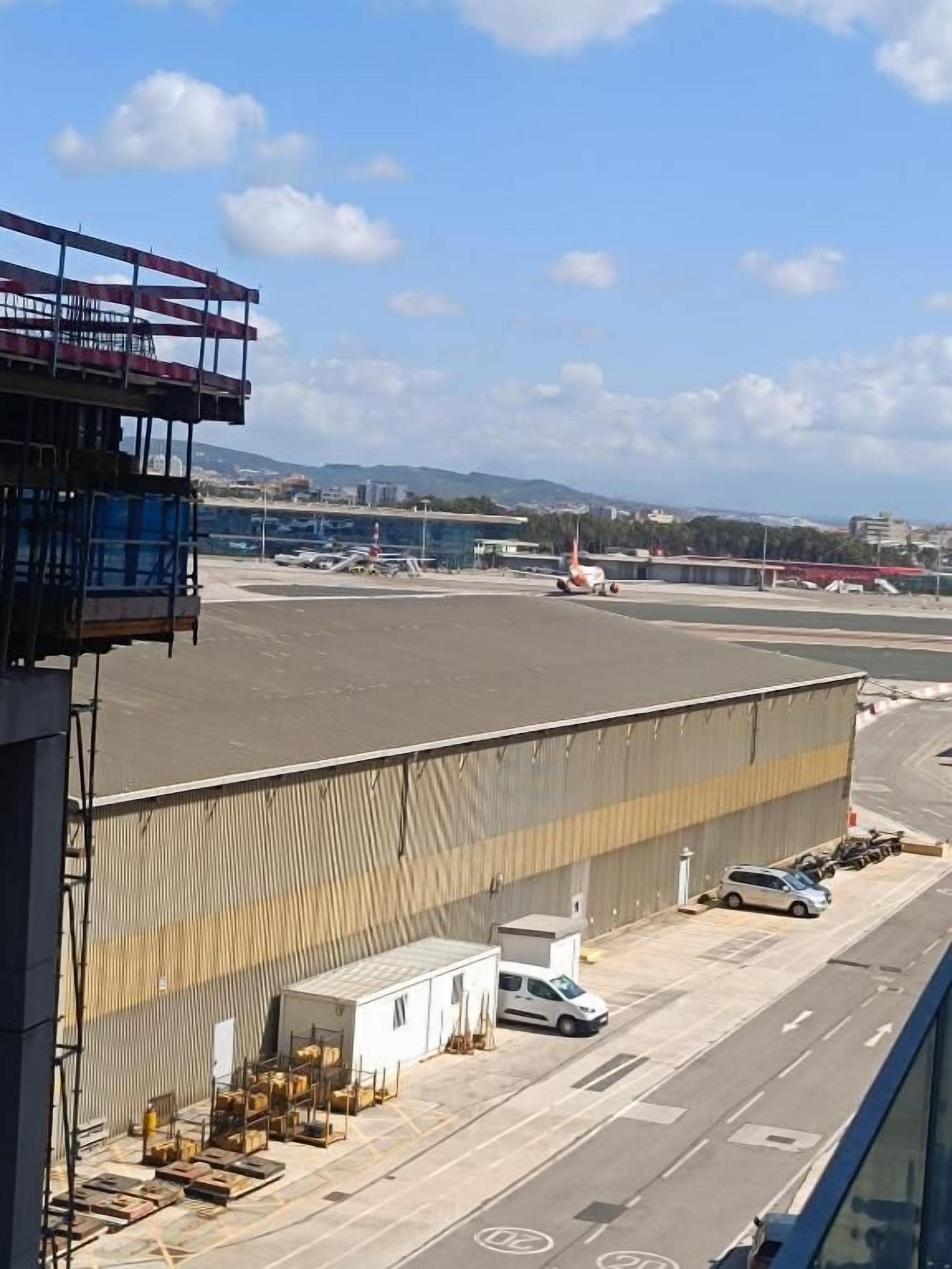 An airport tarmac with a hangar, parked vehicles, and a clear sky.