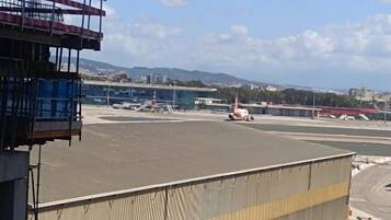An airport tarmac with a hangar, parked vehicles, and a clear sky.