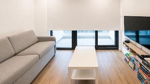 A modern living room with a sofa, a coffee table, a TV, and a bookshelf. - Executive Suite with Swimming Pool & Gym (Gibraltar)