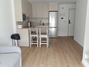 A compact kitchen with a refrigerator, a sink, and a dining area with two chairs.