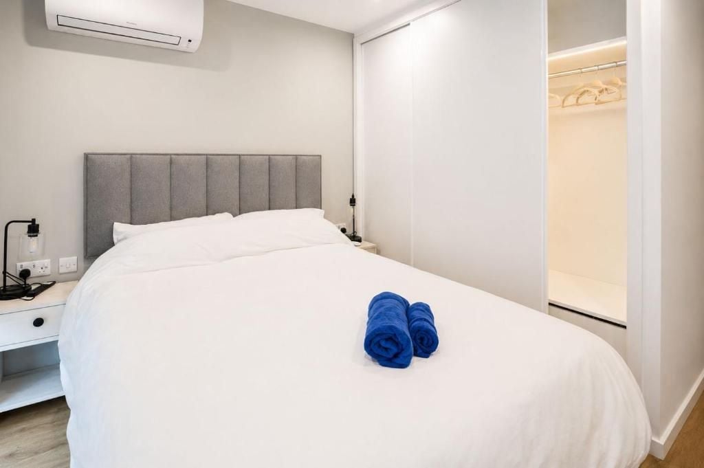 A hotel room with a bed, a bedside table, an air conditioning unit, and a closet.