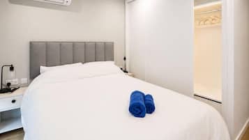 A hotel room with a bed, a bedside table, an air conditioning unit, and a closet.