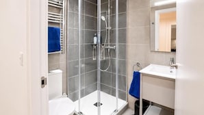 A modern bathroom with a glass-enclosed shower, a white toilet, a sink with a mirror, and a blue towel on the wall. - Executive Suite with Swimming Pool & Gym (Gibraltar)