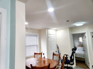 A dining area with a wooden table, chairs, a vase, and a bottle of dish soap.