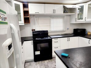 Una cucina compatta con mobili bianchi, un piano cottura nero e un forno a microonde.