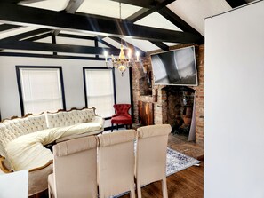 A room with a sofa, chairs, a fireplace, a TV, and a chandelier.