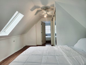 A bedroom with a sloped ceiling, a bed, a ceiling fan, and a skylight.