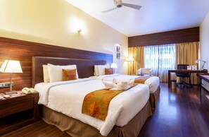 A hotel room with two beds, a desk, a chair, a telephone, and a ceiling fan. - Zip by Spree Hotels at Woodrose Club (Bengaluru)